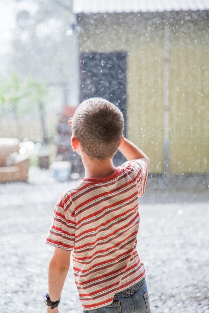 Young boy looking up at falling rain - Australian Stock Image