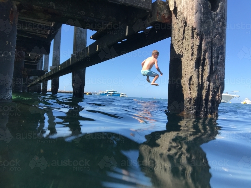 Image of Young boy mid air jetty jumping into ocean taken through piers ...