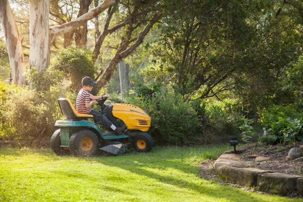 Young boy mowing the front yard on a ride on lawn mower - Australian Stock Image