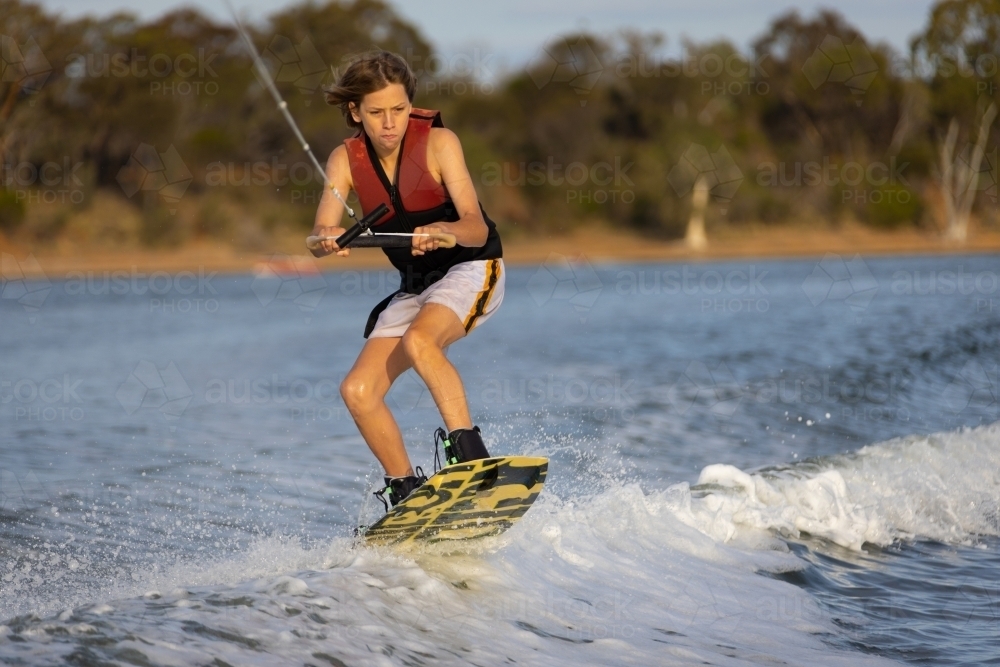 young boy on wake board going over wake - Australian Stock Image