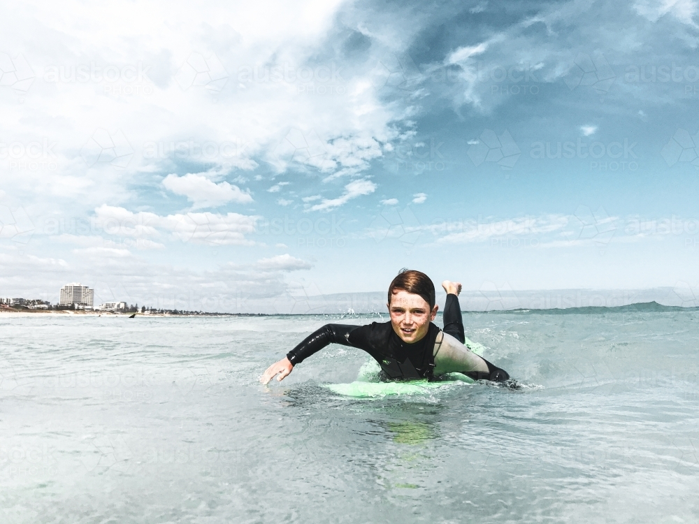 Young boy paddling on surfboard in ocean - Australian Stock Image