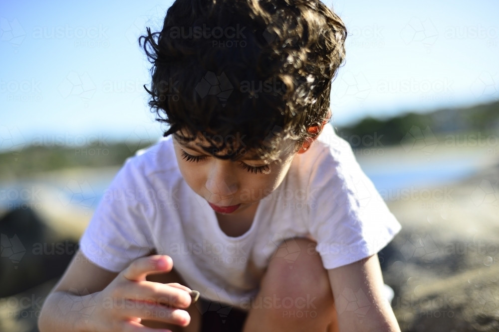 Young boy playing at beach rockpools - Australian Stock Image