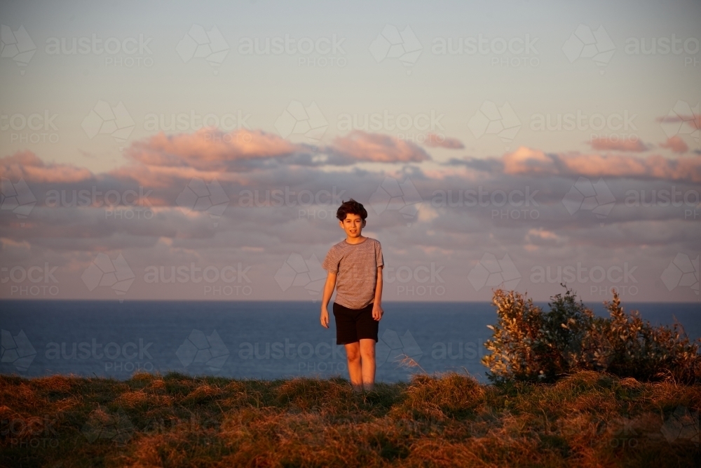 Young boy playing at headland on sunset - Australian Stock Image
