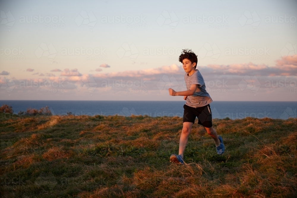 Young boy playing at headland on sunset - Australian Stock Image