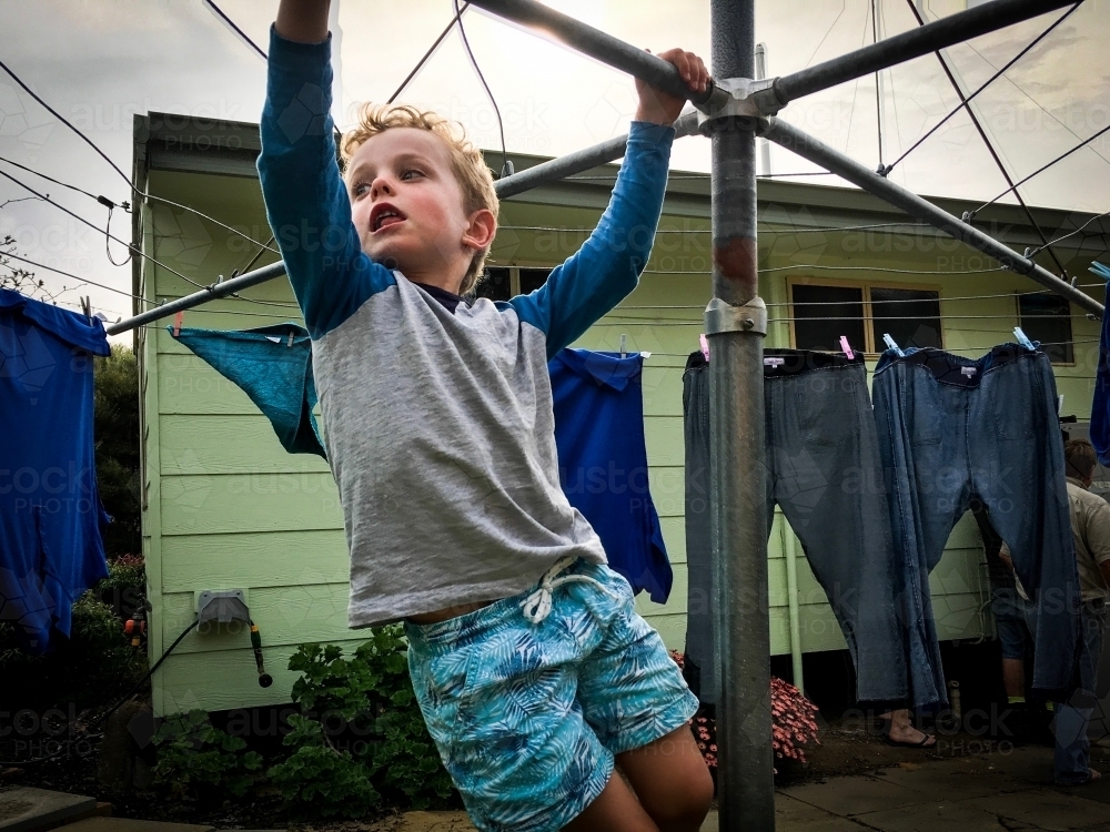 Young boy playing on hills hoist in front of weatherboard house - Australian Stock Image