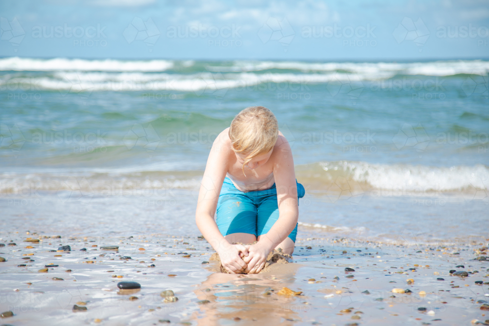 Young boy playing on the beach digging in the sand - Australian Stock Image