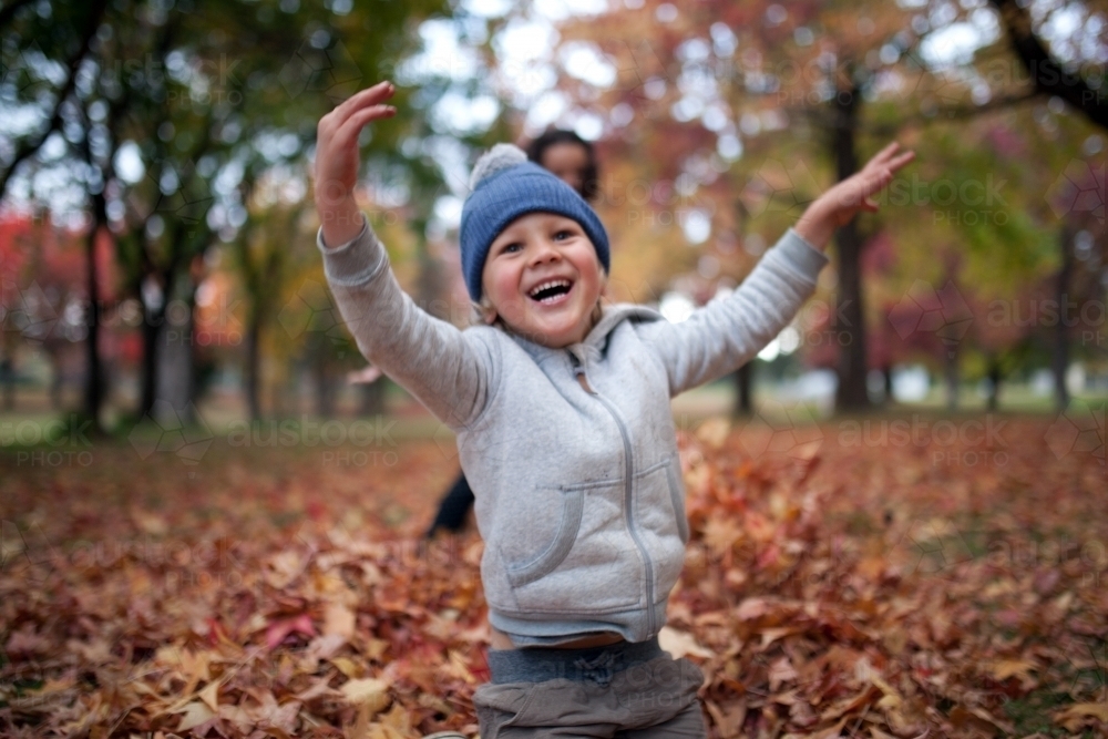 Young boy playing outdoors among piles of autumn leaves - Australian Stock Image