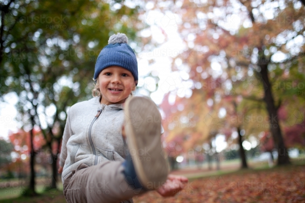 Young boy playing outdoors among piles of autumn leaves - Australian Stock Image