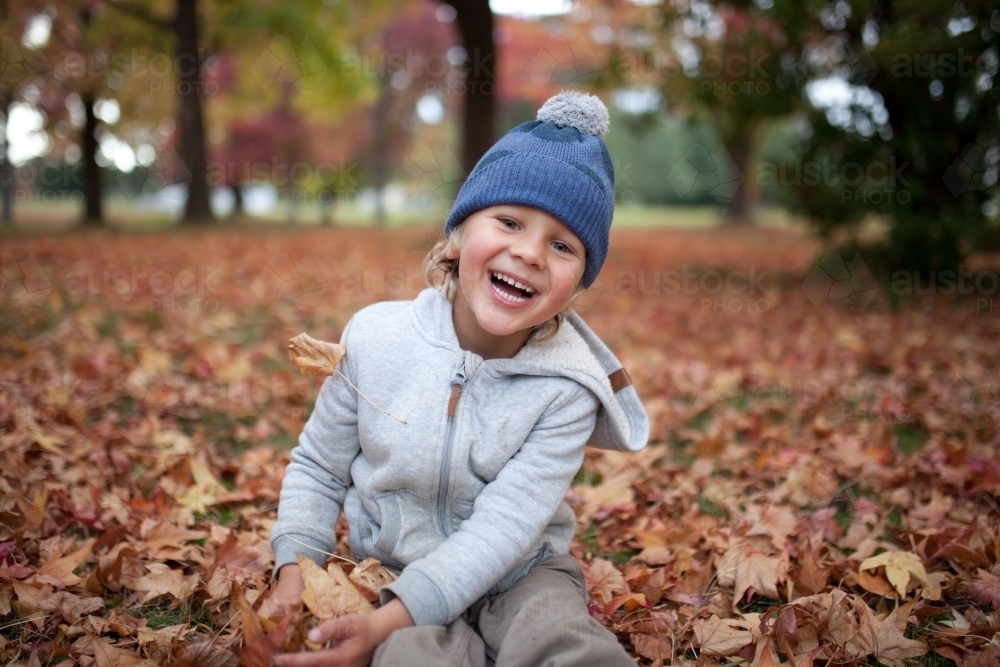 Young boy playing outdoors among piles of autumn leaves - Australian Stock Image