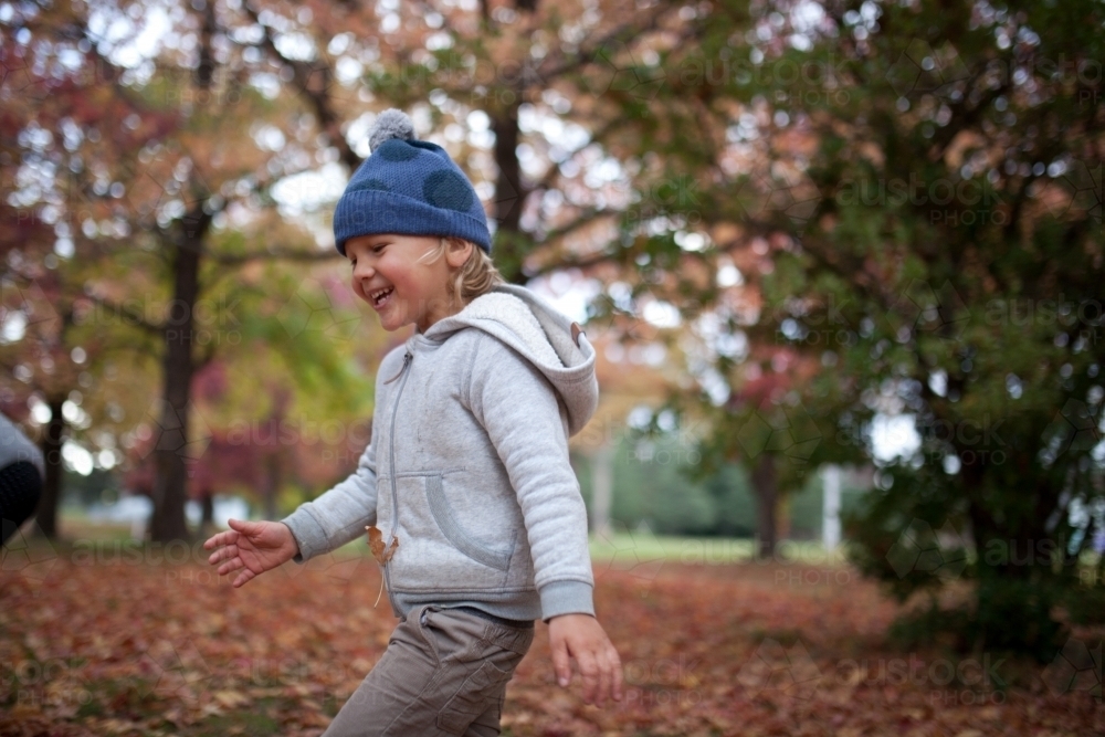 Young boy playing outdoors among piles of autumn leaves - Australian Stock Image