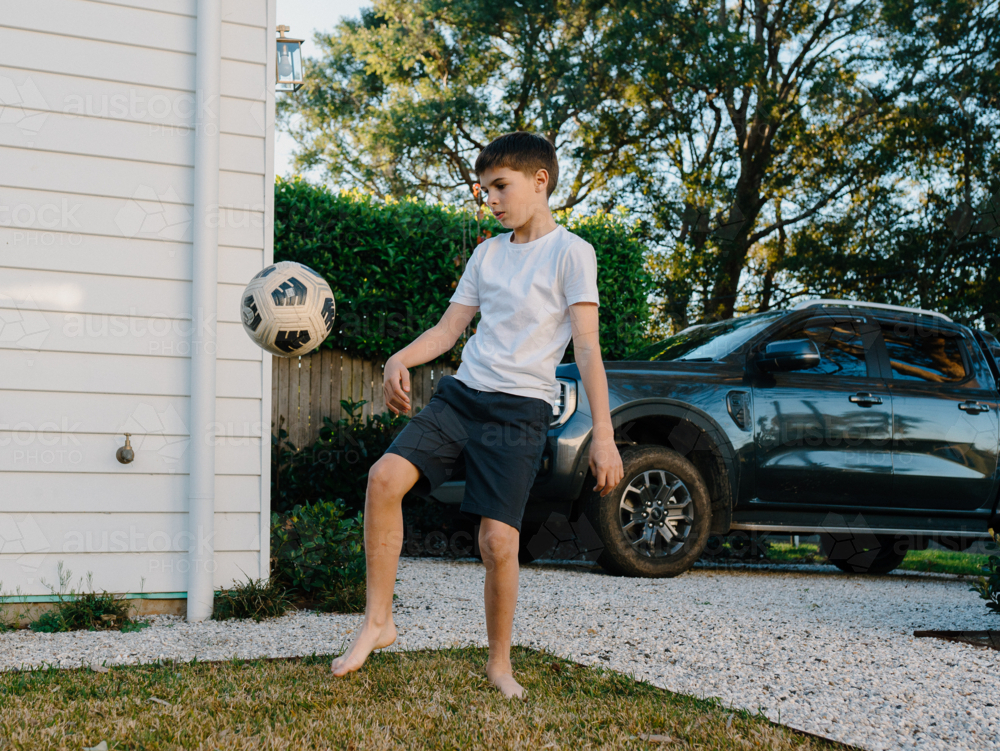 Young boy playing soccer outside in yard - Australian Stock Image