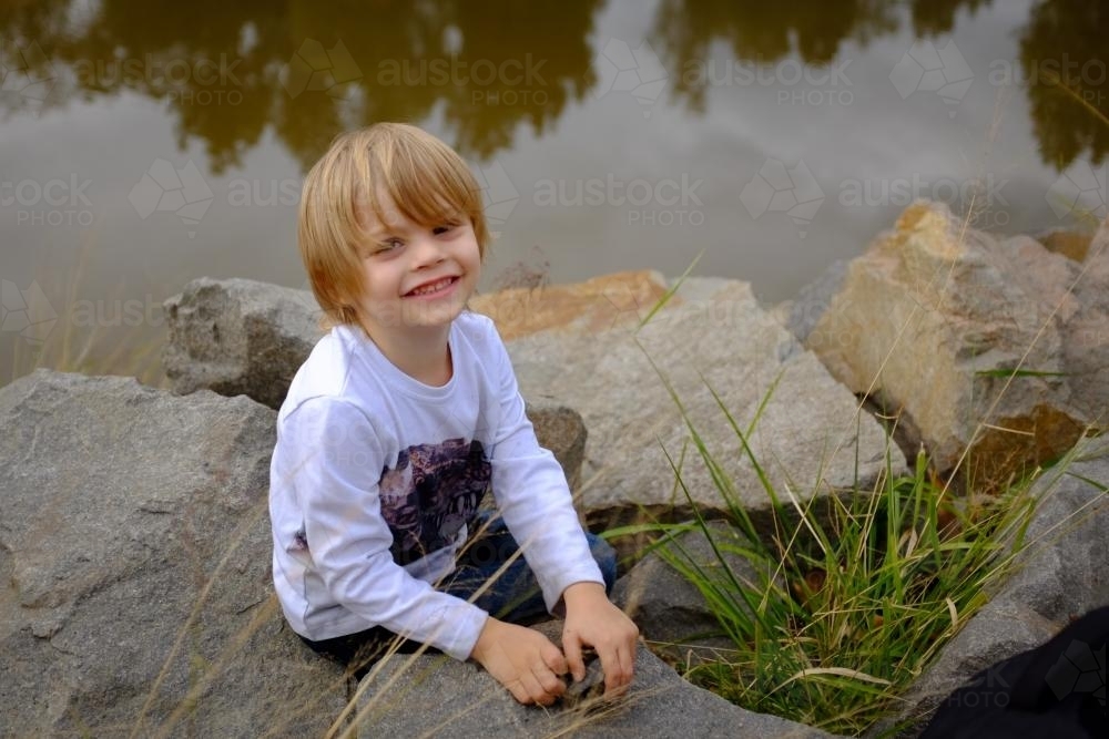 Young boy playing with rocks by the water - Australian Stock Image