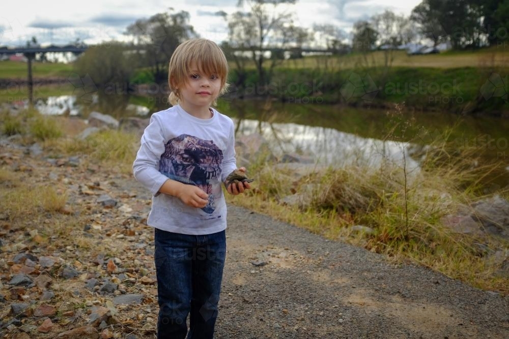Young boy playing with rocks by the water - Australian Stock Image