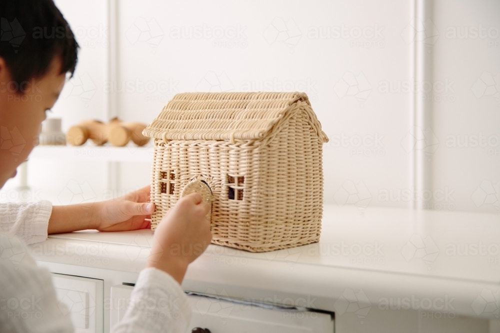 Young boy playing with small toy house with wooden car toy in the background - Australian Stock Image