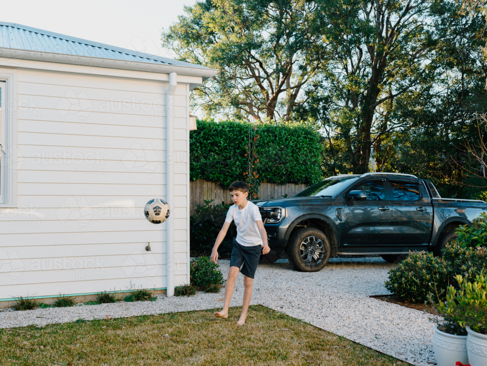Young boy playing with soccer ball in suburban yard - Australian Stock Image