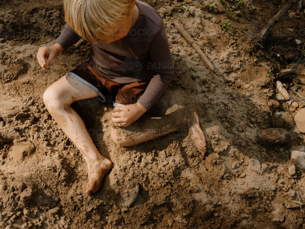 young boy playing with soil while sitting on the ground - Australian Stock Image