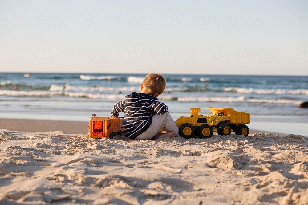 Young boy playing with toy trucks on the beach - Australian Stock Image
