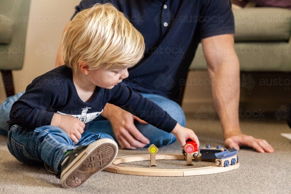 Young boy playing with wooden toy train on the floor - Australian Stock Image