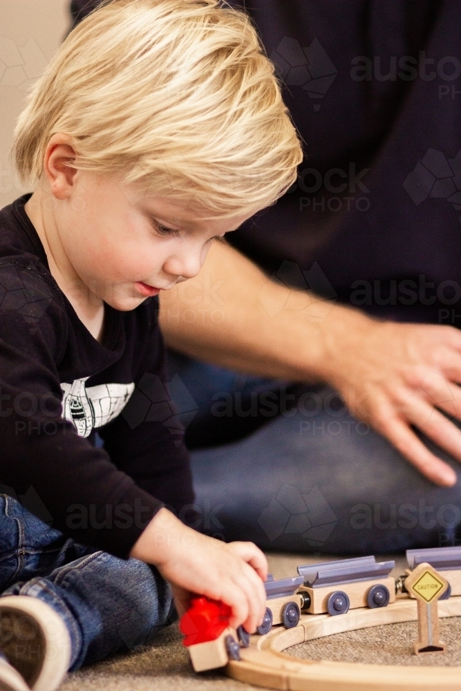 Young boy playing with wooden toy train on the floor - Australian Stock Image