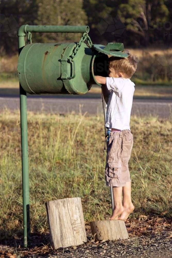 Young boy reaching to check for mail in the milk can mailbox - Australian Stock Image