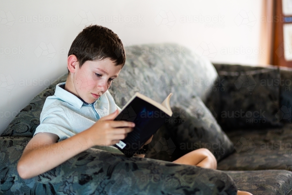 Young boy reading a book at home - Australian Stock Image