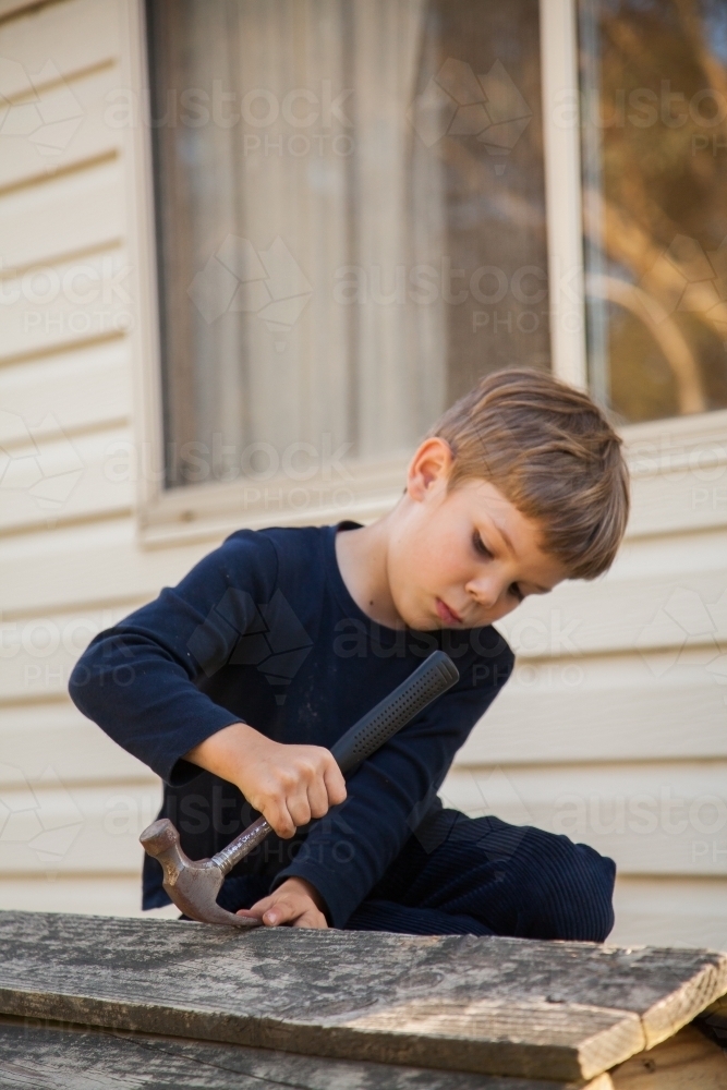 Young boy repairing cubbyhouse with nails - Australian Stock Image