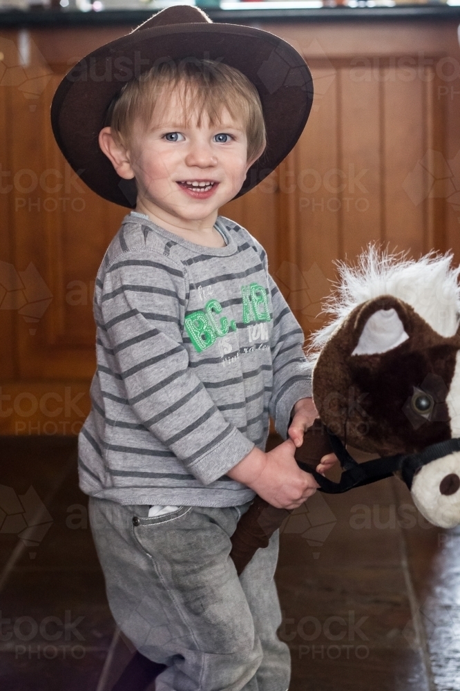 Young boy riding toy horse and smiling for camera - Australian Stock Image