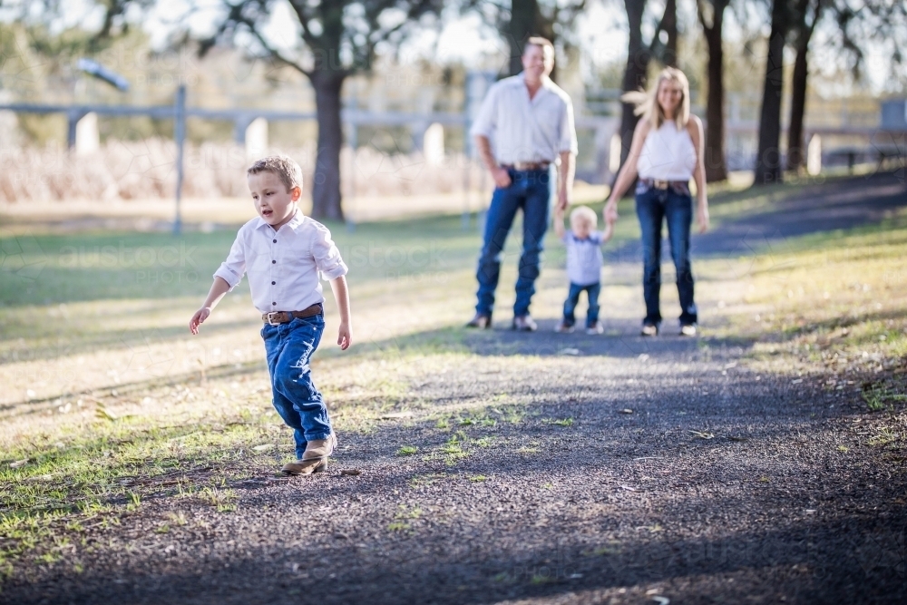 Young boy running ahead of parents holding hands of little brother - Australian Stock Image