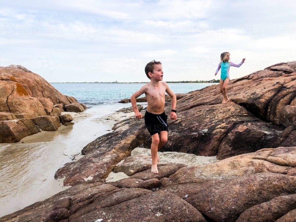 Young boy running over coastal rocks with young girl following him - Australian Stock Image