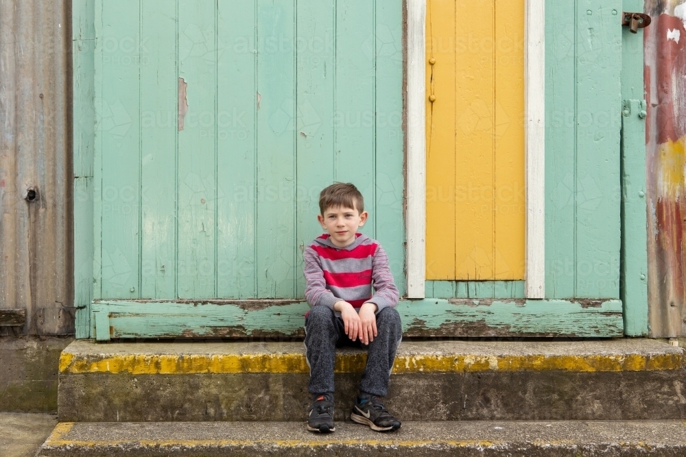 Young boy sitting in front of yellow door - Australian Stock Image