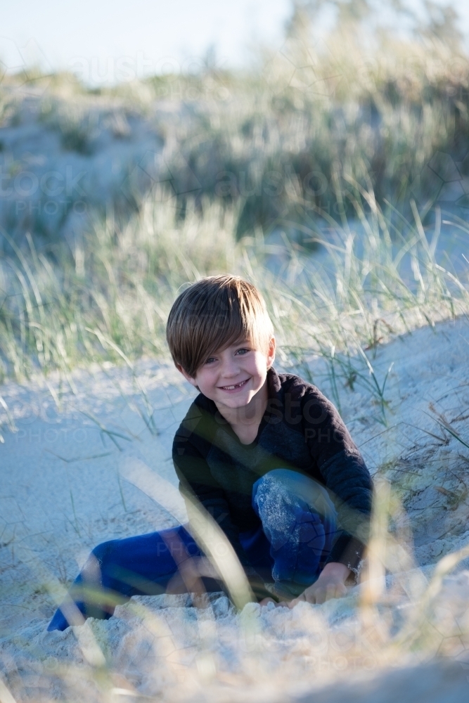 Image of Young boy sitting in the sand dunes smiling - Austockphoto