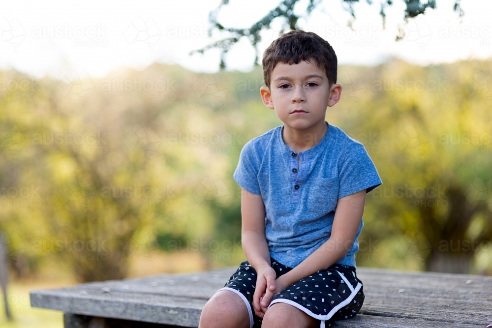 Young boy sitting on bench with nature behind - Australian Stock Image