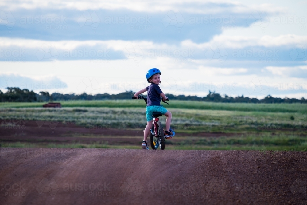 Young boy sitting on bike at crest of a hill in rural setting - Australian Stock Image