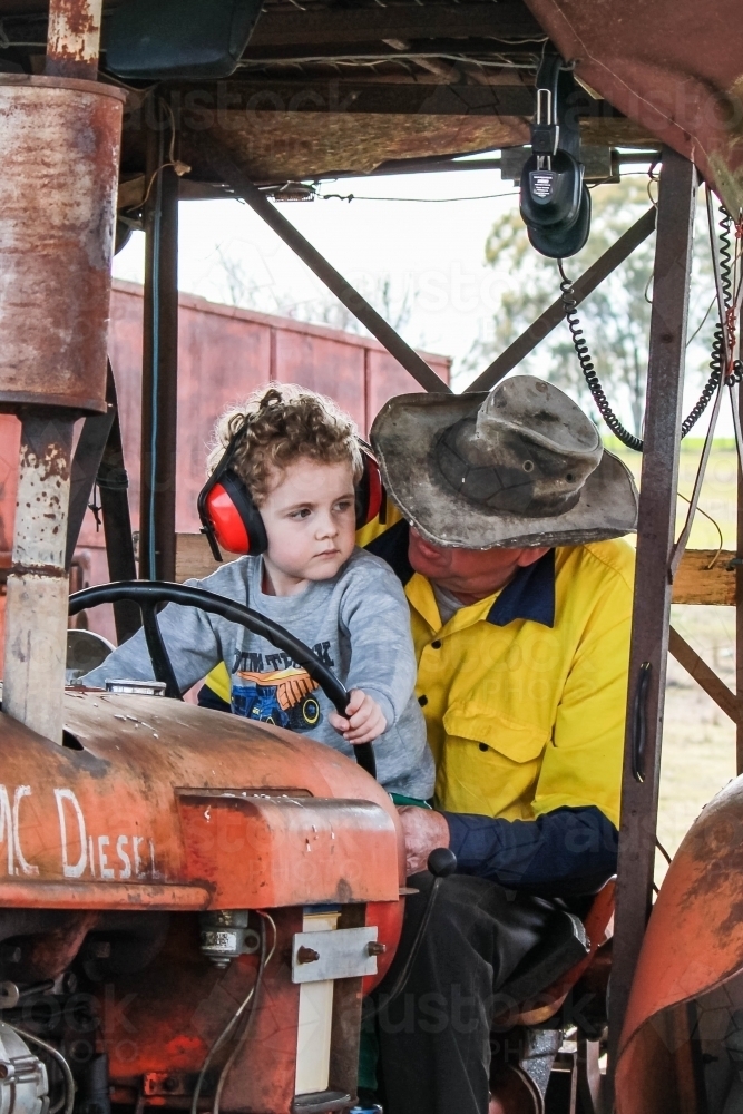 Young boy sitting on lap of farmer on tractor - Australian Stock Image