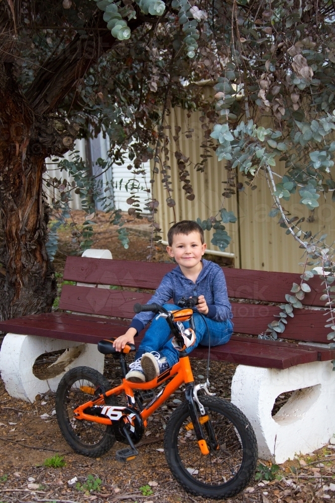 Young boy sitting on park bench with bike - Australian Stock Image