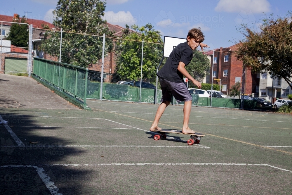 Young boy skating in a basketball court - Australian Stock Image