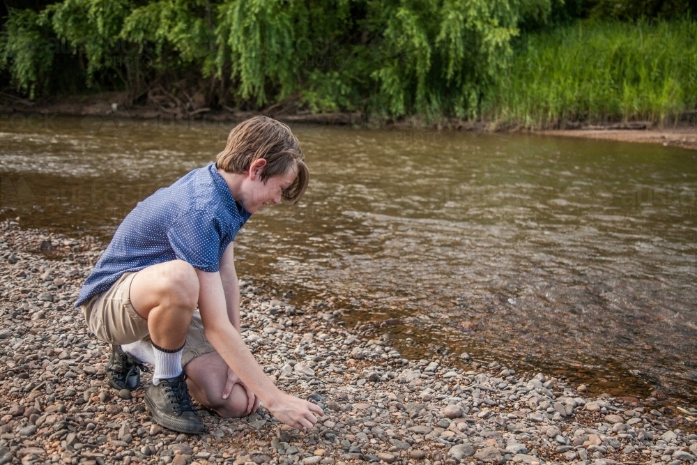 Image of Young boy skimming stones beside a river - Austockphoto