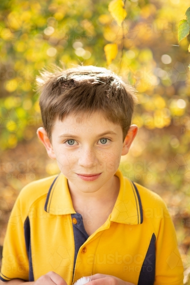 Young boy smiling at camera in yellow school uniform - Australian Stock Image
