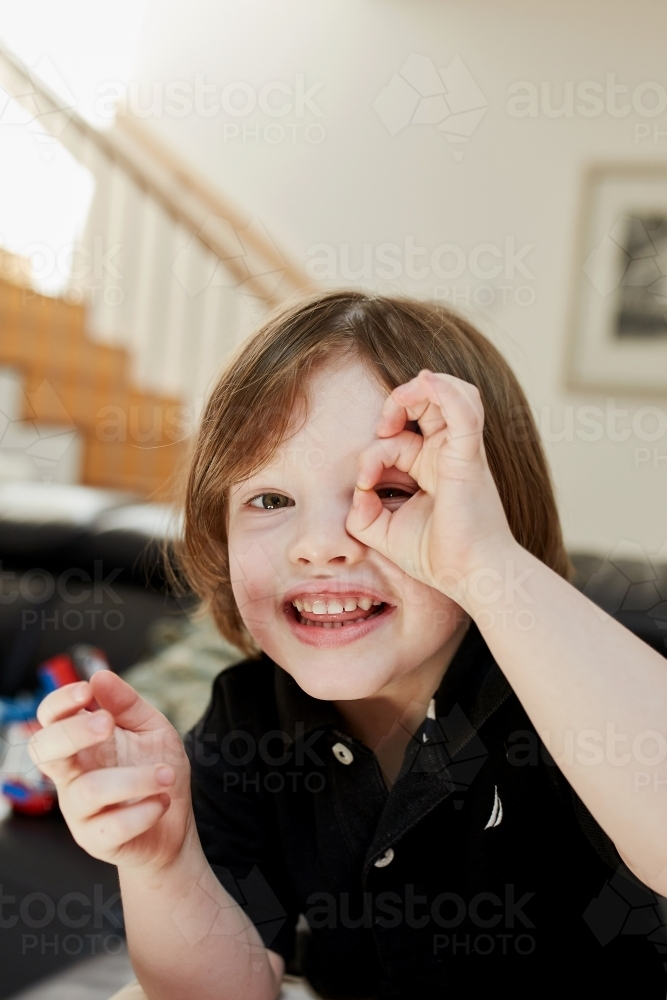 Young boy smiling peeping through his finger holes - Australian Stock Image