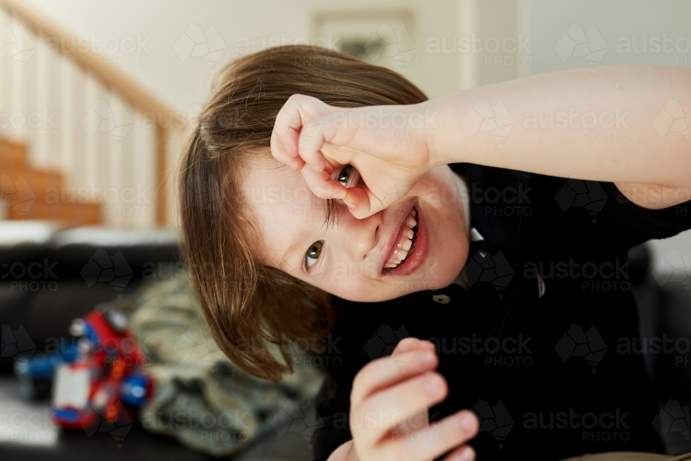 Young boy smiling peeping through his finger holes - Australian Stock Image