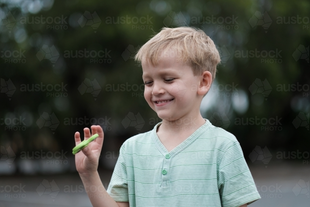 Young boy smiling playing with fidget spinner - Australian Stock Image