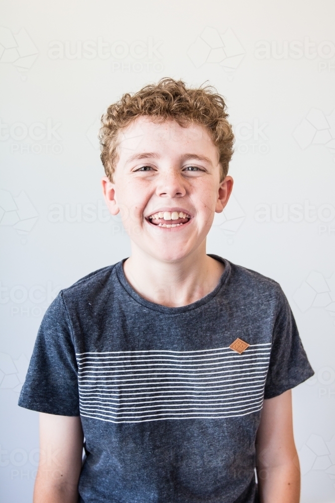 Young boy smiling with curly hair standing white background - Australian Stock Image