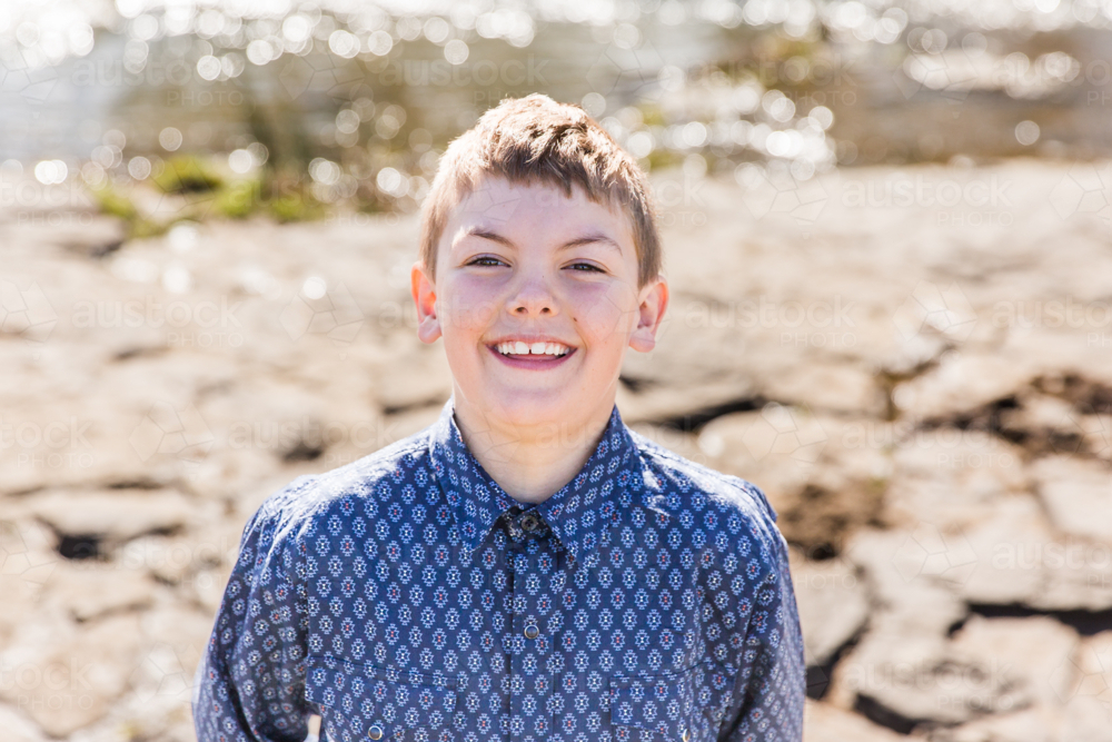 Young boy smiling with rocks and water in background - Australian Stock Image