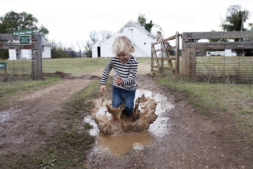 Young boy splashing in muddy puddle on the farm - Australian Stock Image