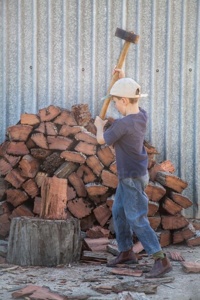 Young boy splitting wood for the fire with a axe - Australian Stock Image
