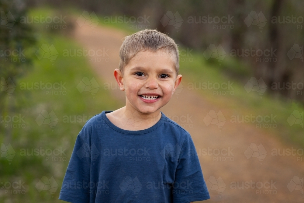 Young boy standing along the dirt road smiling - Australian Stock Image