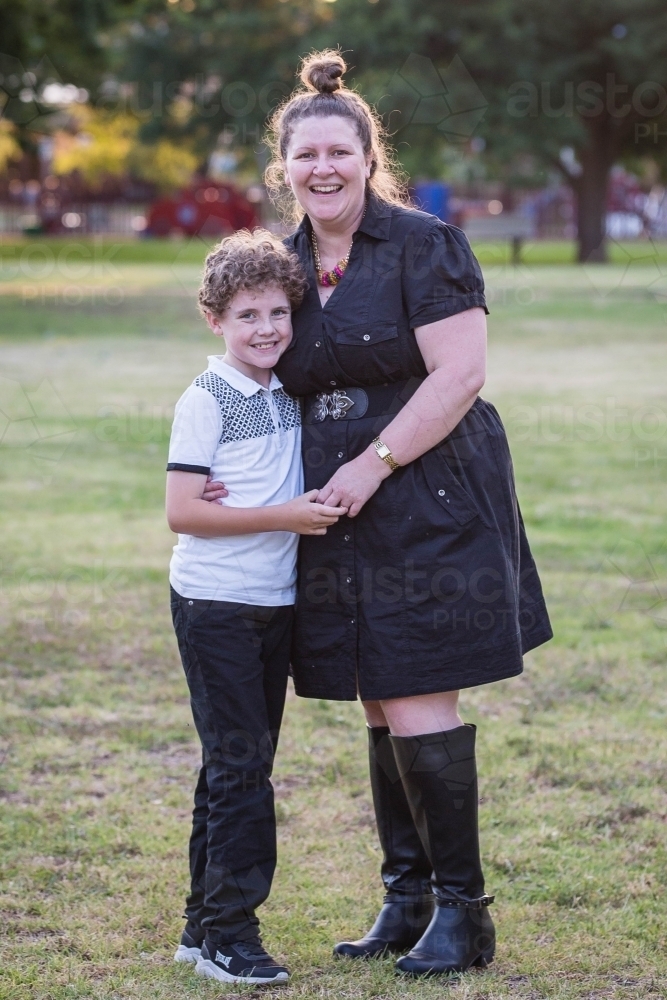 Young boy standing holding hands with mother smiling - Australian Stock Image