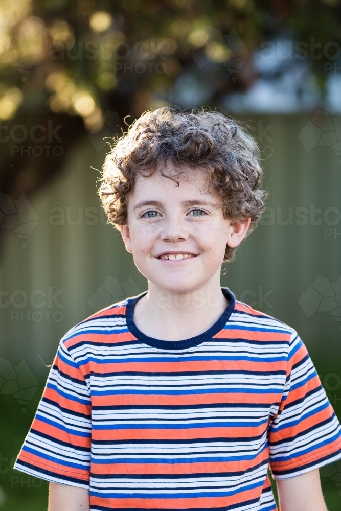 Young boy standing in yard smiling with backlight - Australian Stock Image