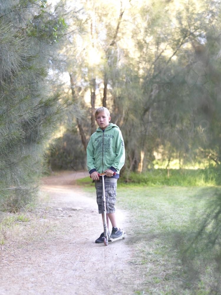Young boy standing with scooter on bush track - Australian Stock Image