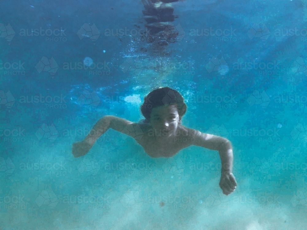 Young boy swimming underwater with sun beams through water - Australian Stock Image